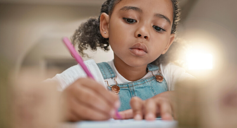 Close up of a young girl holding a pencil and concentrating on writing in a notebook 